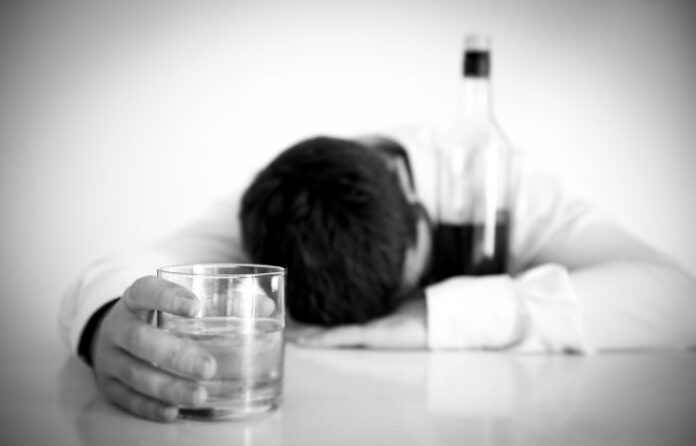 black and grey image of a businessman asleep with alcohol to symbolize executive mental-health and substance-abuse issues