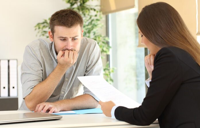 AN anxious man listens as a female reads to him from a clipboard for understanding the theory of anxiety and stress at work