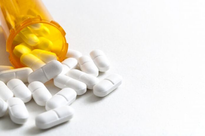 A bottle of white pills spilling onto a table signifies the opioid crisis at work